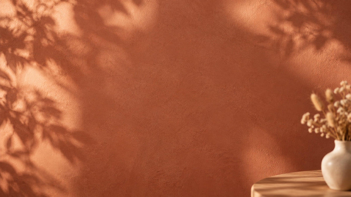 Mur terracotta baigné de lumière chaude, ombre de feuillage et vase de fleurs séchées